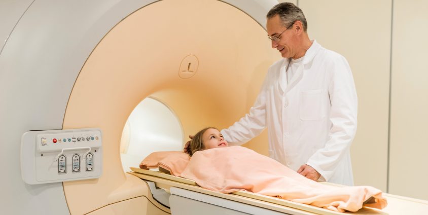 child laying down on MRI scanning table with physician looking over her
